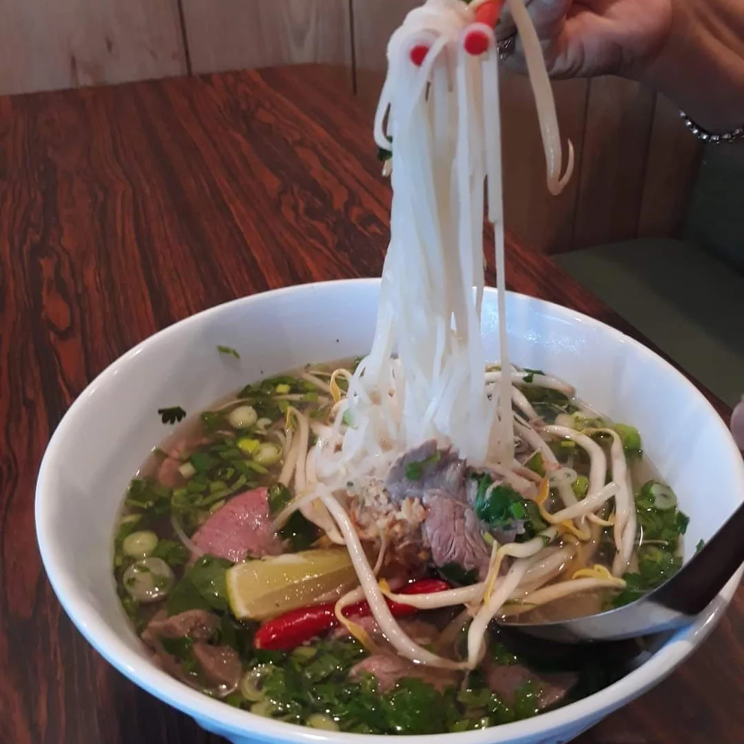 A bowl of pho with noodles being lifted by chopsticks.