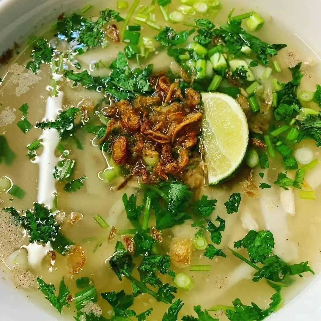 A bowl of noodle soup with herbs, lime, and fried onions.