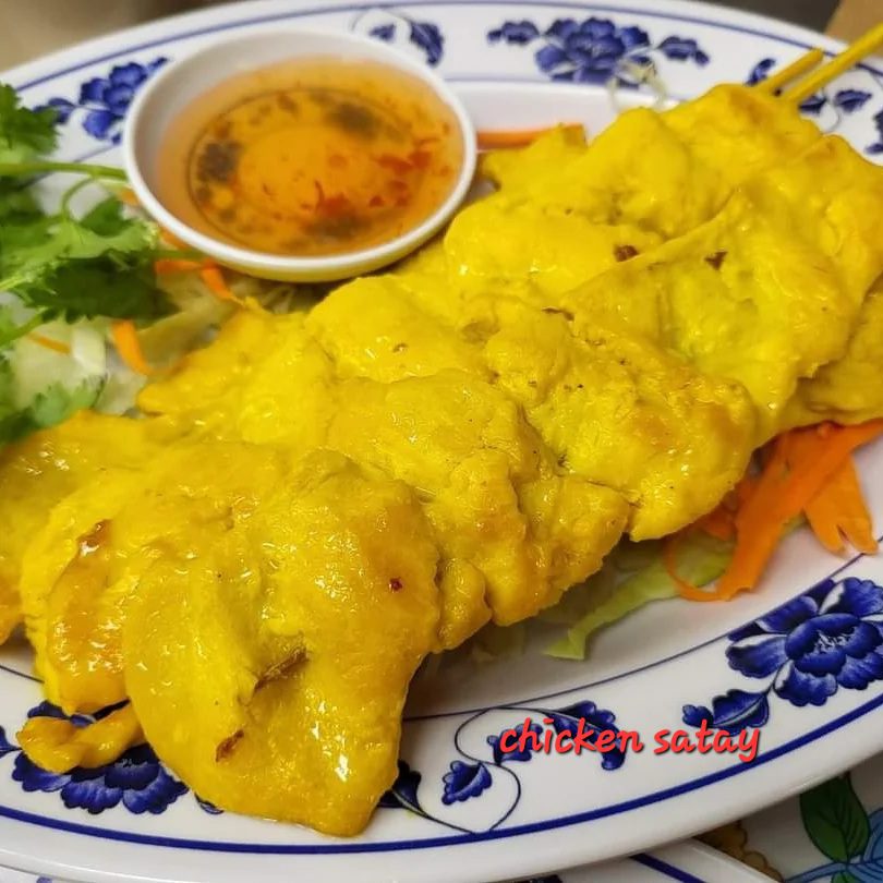 A plate of yellow chicken satay with peanut sauce and garnishes.