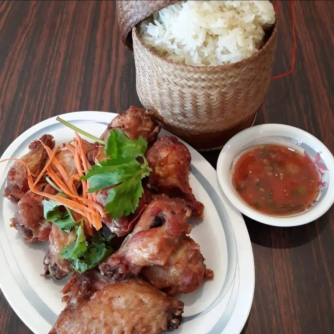 Fried chicken with sticky rice in a bamboo container and spicy sauce on a wood table.