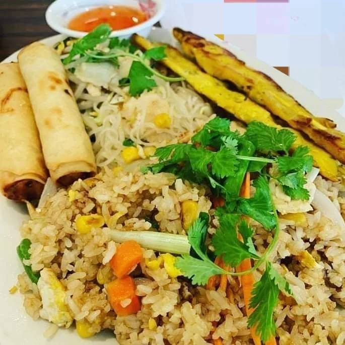 Plate of fried rice with vegetables, spring rolls, grilled plantains, and sauce on the side.