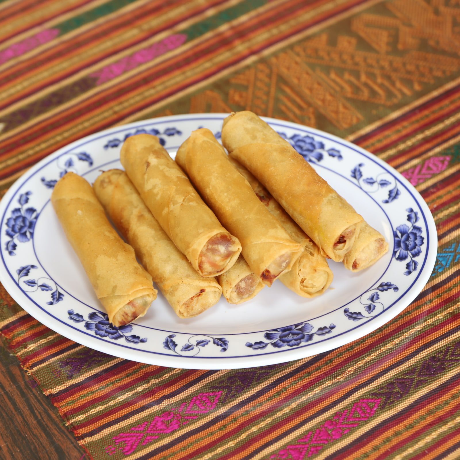 A plate of spring rolls on a colorful woven tablecloth.