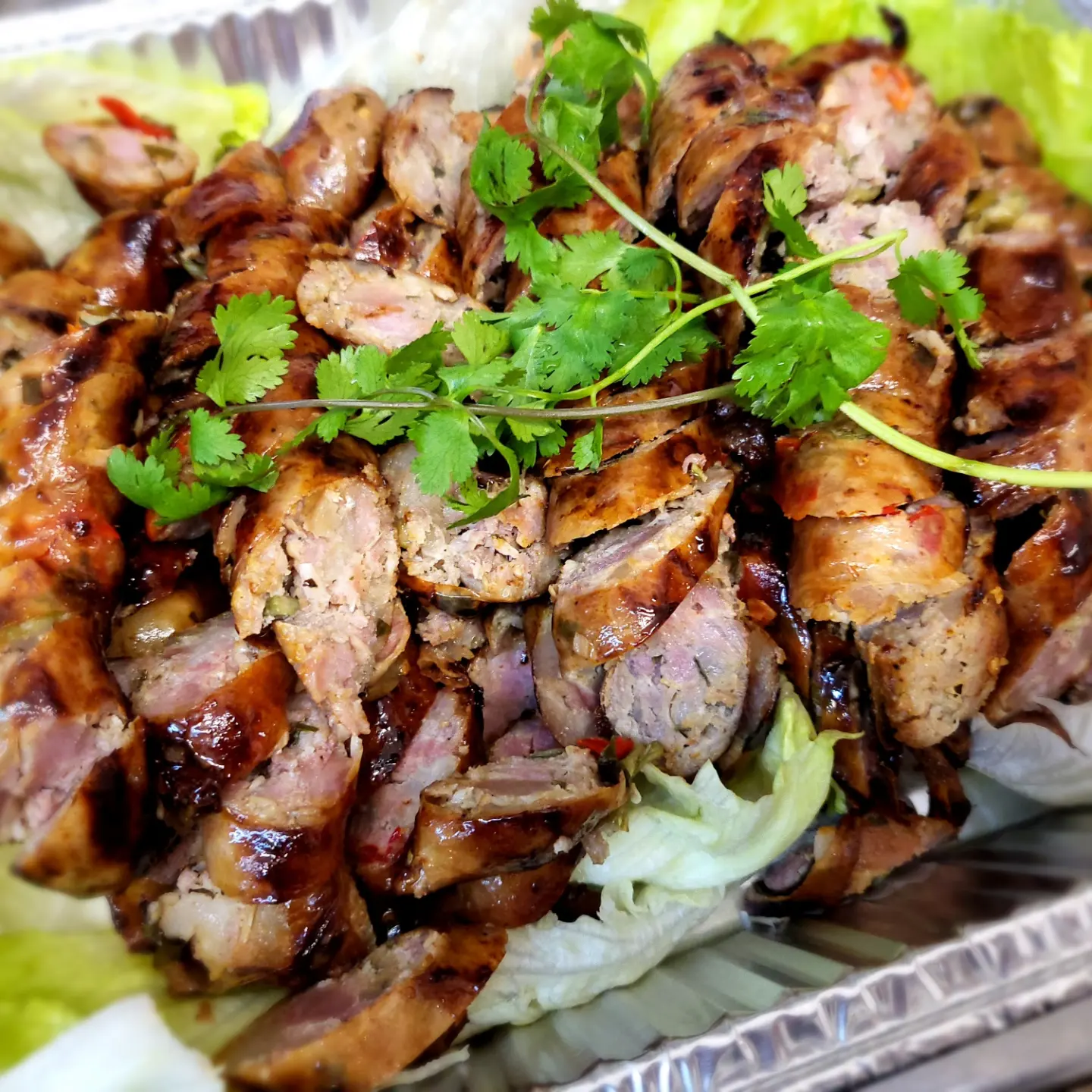 Sliced grilled sausage with herbs on lettuce in a tray.