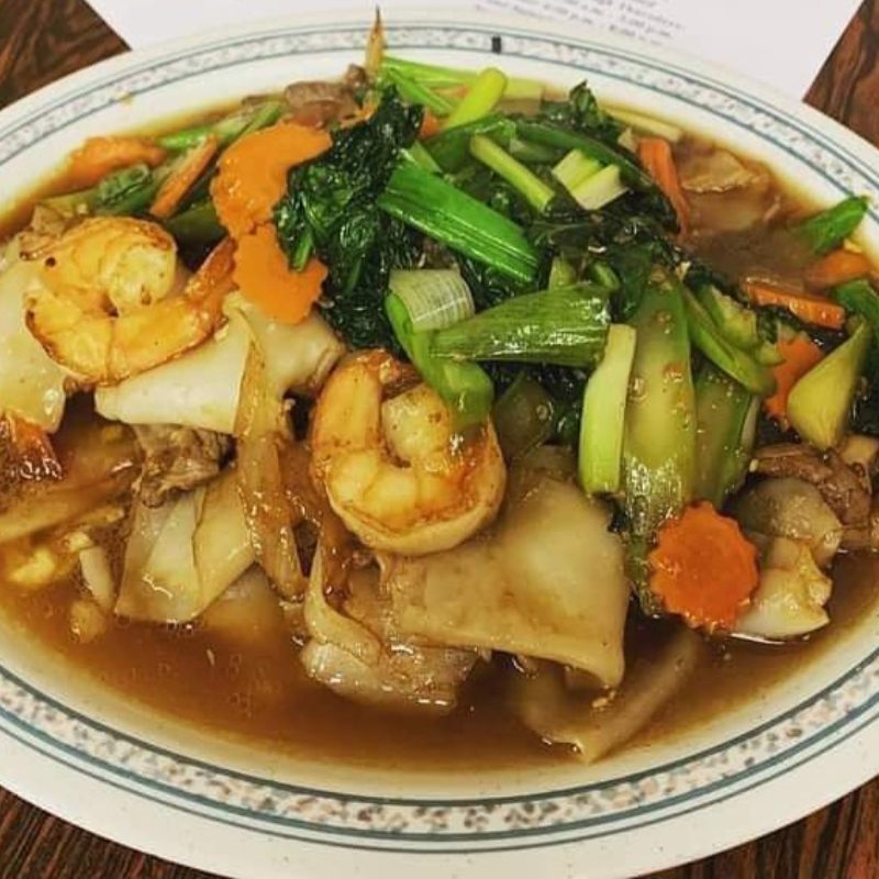 A bowl of noodle soup with shrimp, vegetables, and flat noodles.