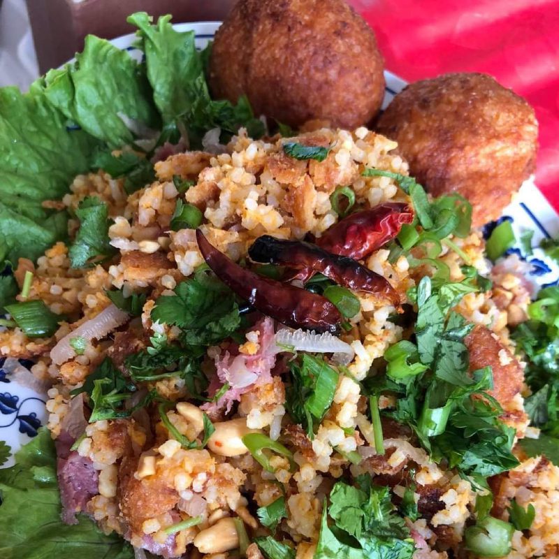 A plate of bulgur pilaf with herbs, nuts, and two fried balls, garnished with lettuce leaves.