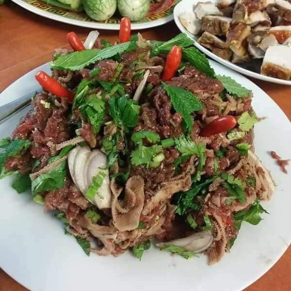 A plate of spicy beef salad with herbs, onions, and chili peppers, surrounded by other dishes.