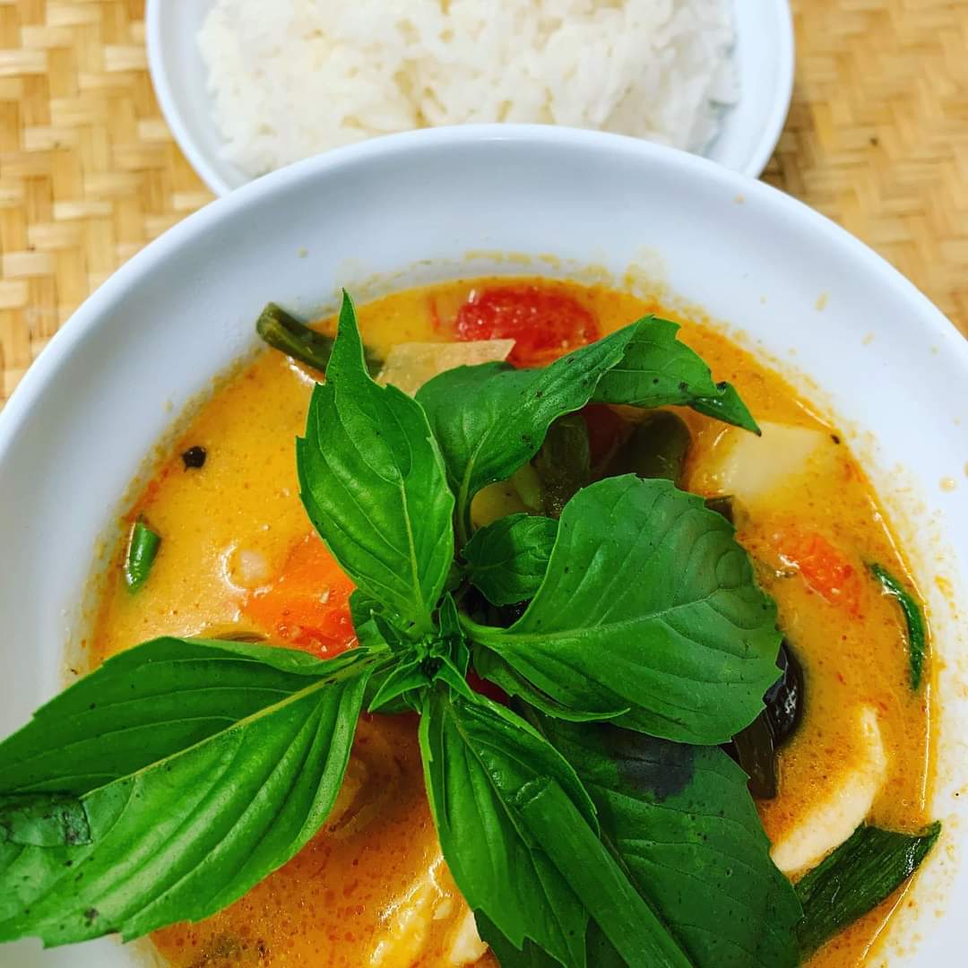 Thai curry with basil on top and a side of rice in the background.