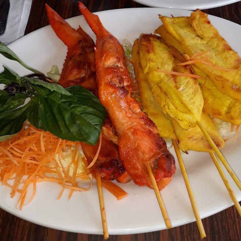 Grilled shrimp skewers and sliced fried plantains on a plate, garnished with basil and carrots.