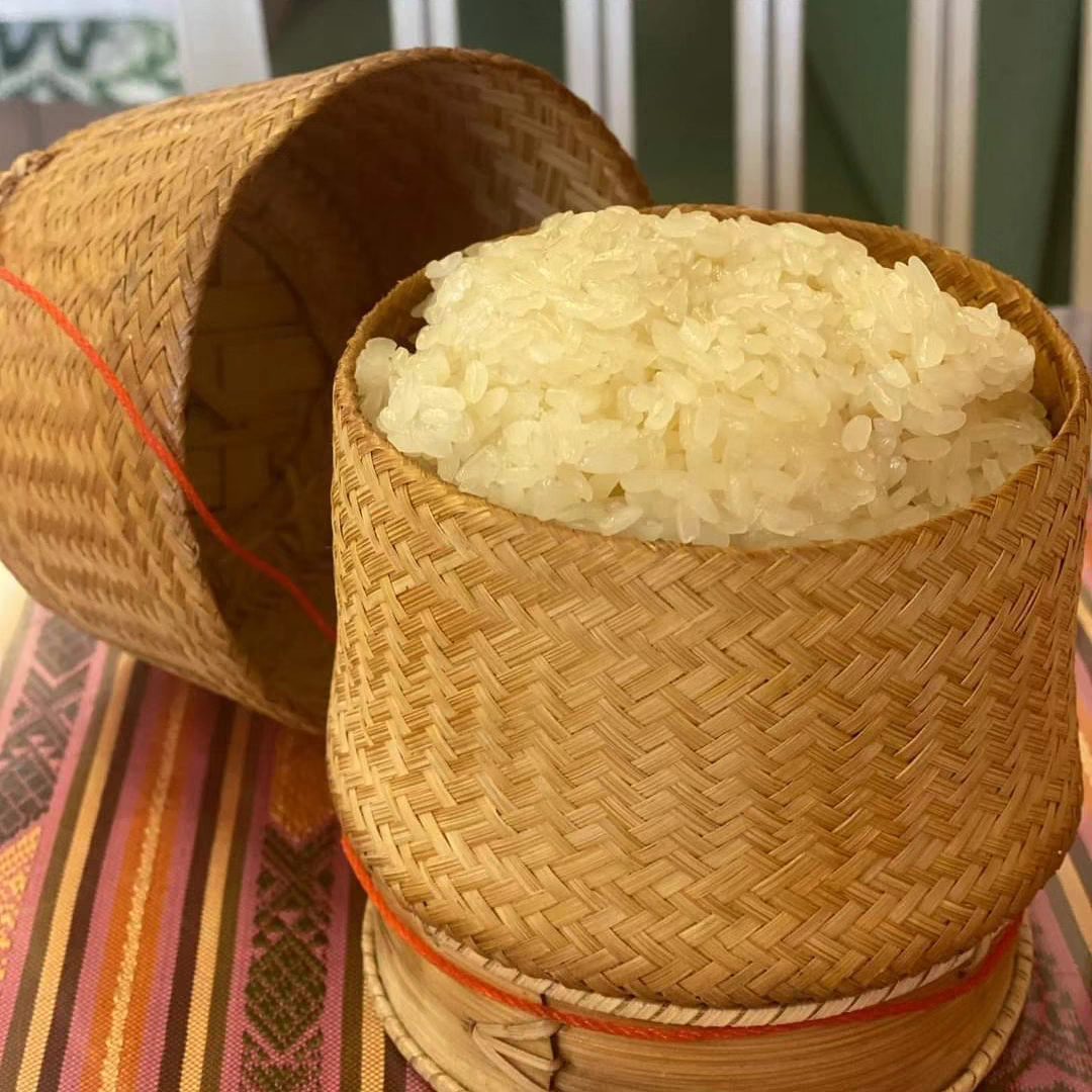 Sticky rice in a traditional woven bamboo basket, lid askew.