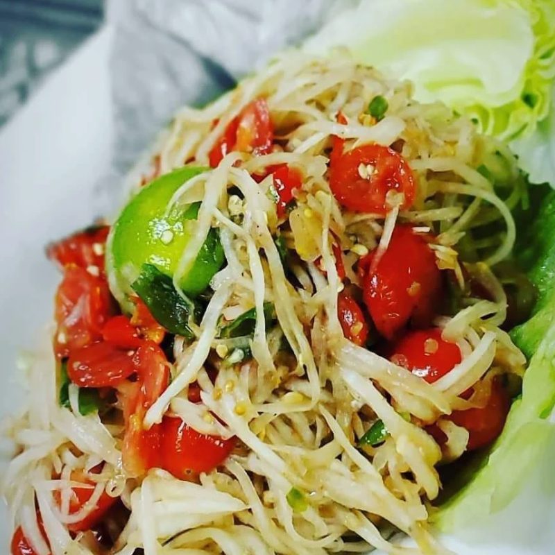 A plate of papaya salad with cherry tomatoes, lime, and lettuce on the side.